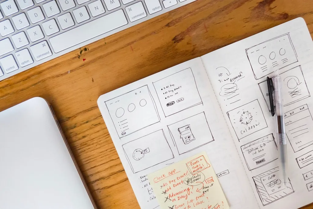 Open notebook of app wireframes beside a laptop, planning product pages before real data
