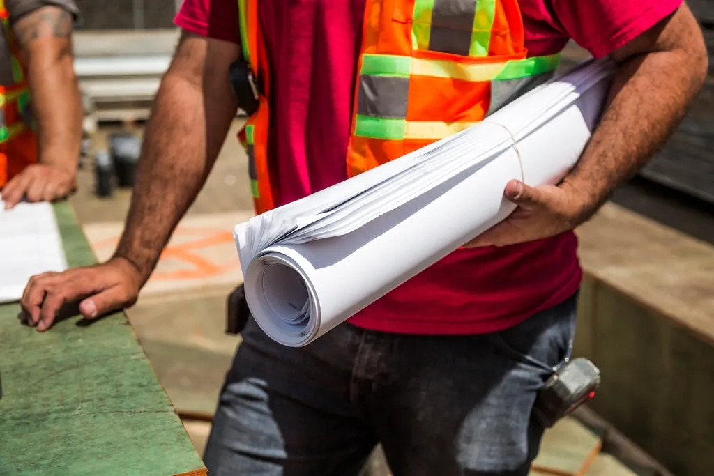 Worker holding rolled up building plans, one blueprint shared by every team