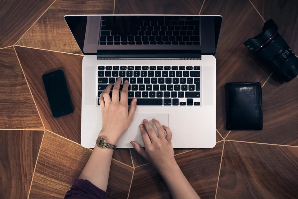 Hands typing on a laptop beside a phone and wallet, writing a rate increase notice